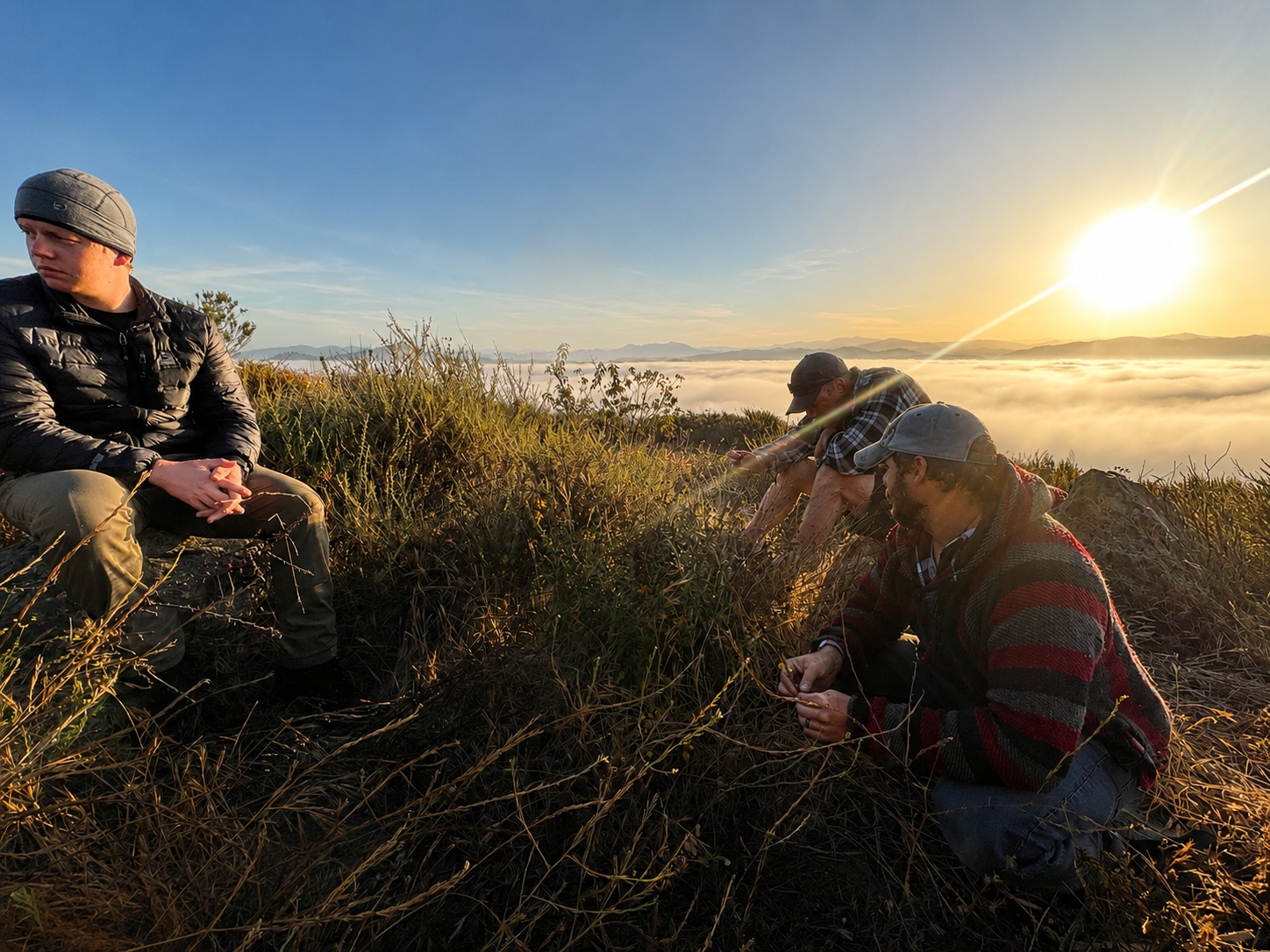 Three S.O.S. retreat participants sit quietly above a valley at sunrise.